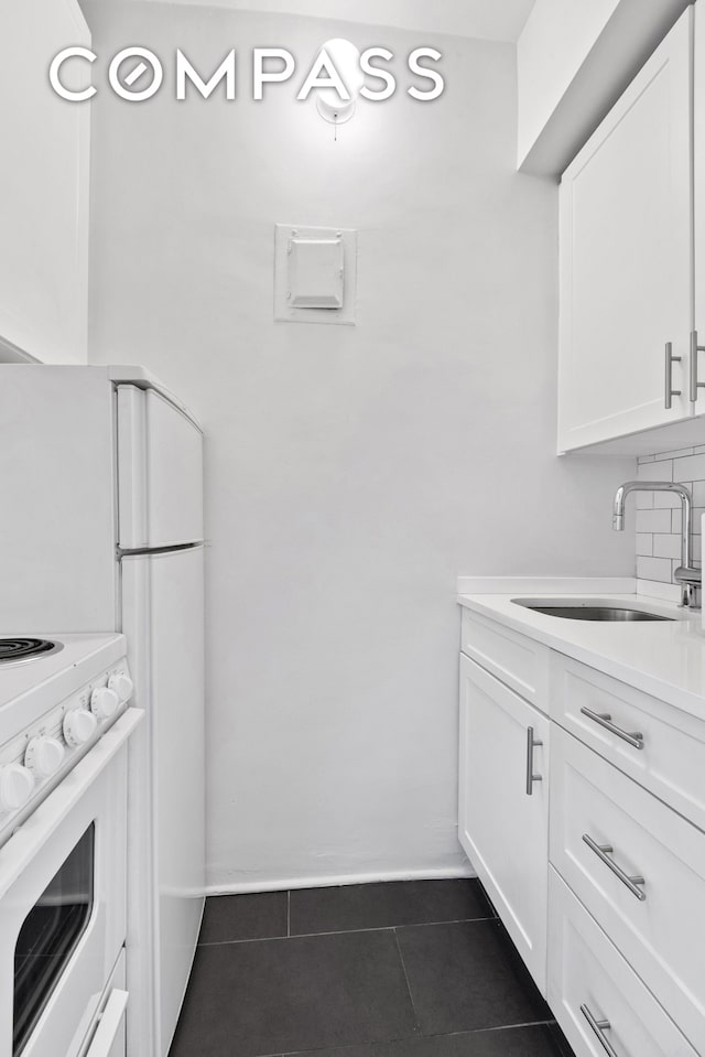 kitchen featuring dark tile patterned flooring, a sink, white cabinets, backsplash, and white range with electric cooktop