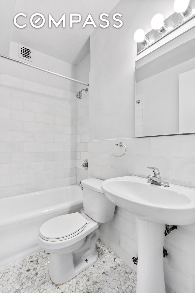 full bathroom featuring tile walls, visible vents, toilet, wainscoting, and tub / shower combination