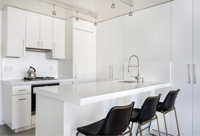 kitchen with a kitchen bar, stainless steel gas stovetop, sink, and white cabinetry