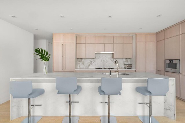 kitchen with an island with sink, light brown cabinetry, and a breakfast bar area