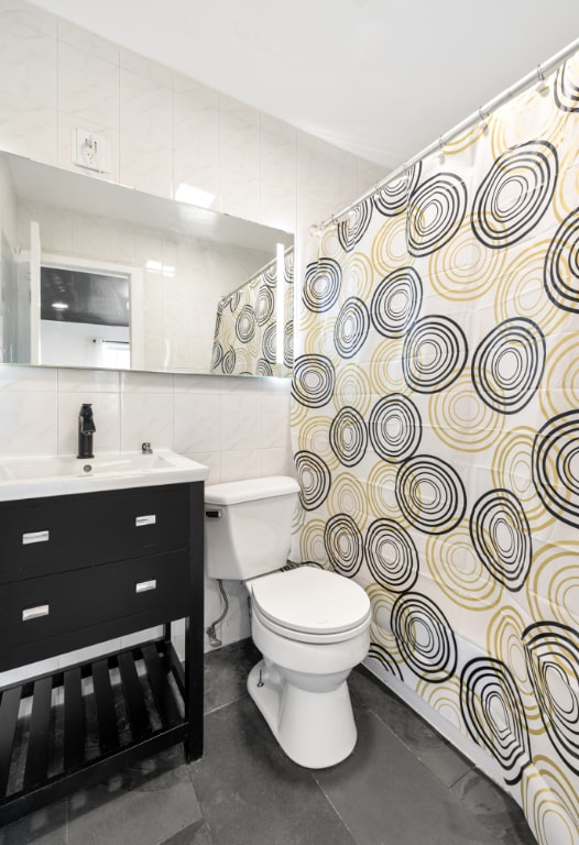 bathroom featuring tile patterned floors, vanity, backsplash, tile walls, and toilet