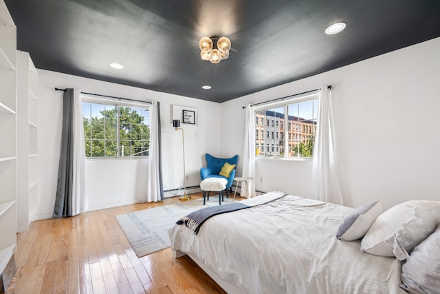 bedroom featuring a baseboard radiator, light hardwood / wood-style floors, and multiple windows