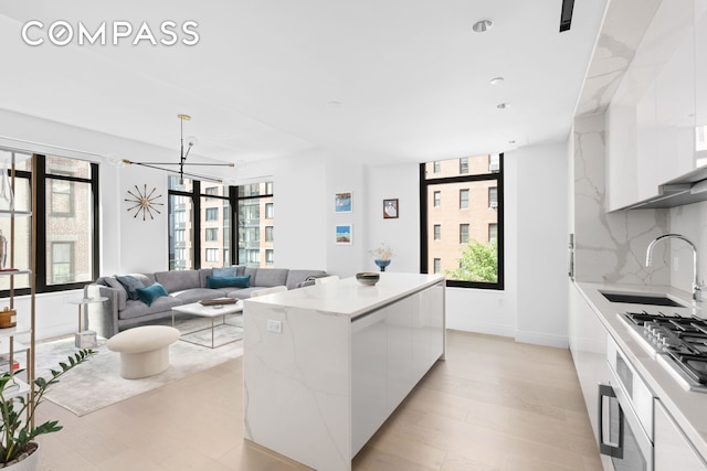 kitchen featuring modern cabinets, a sink, backsplash, a kitchen island, and white cabinetry