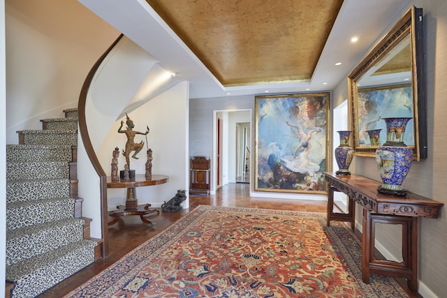 corridor with recessed lighting, stairs, a tray ceiling, and wood finished floors
