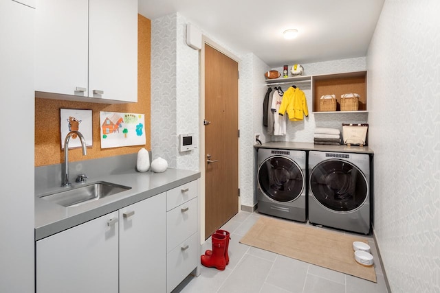 clothes washing area with a sink, tile patterned floors, washing machine and dryer, and cabinet space