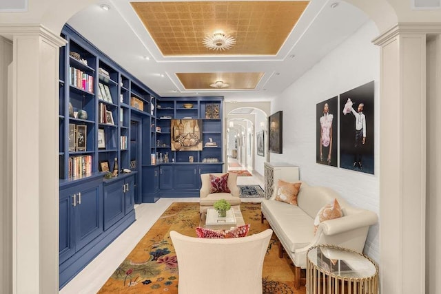 sitting room featuring arched walkways, a raised ceiling, built in features, and ornate columns