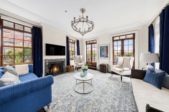 living room with a notable chandelier, crown molding, a high end fireplace, and french doors