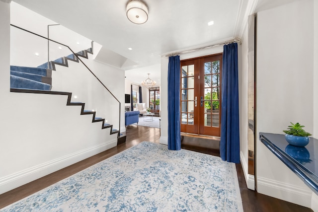 foyer entrance featuring dark wood-type flooring, crown molding, french doors, and a notable chandelier