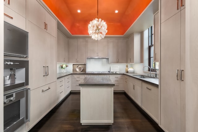 kitchen featuring sink, a tray ceiling, a kitchen island, decorative light fixtures, and stainless steel oven