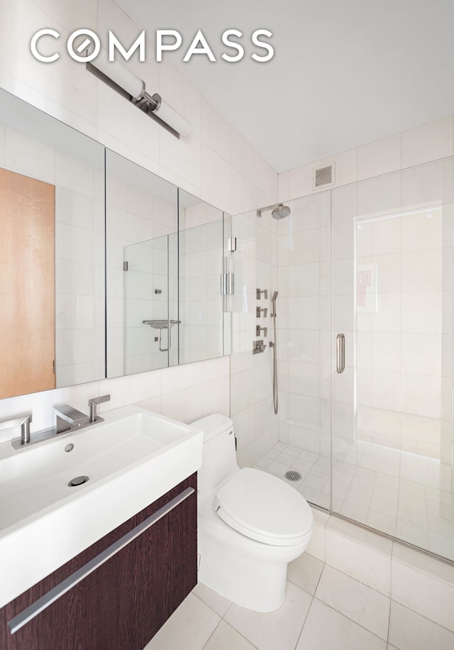 full bathroom with toilet, vanity, a stall shower, tile patterned floors, and tile walls