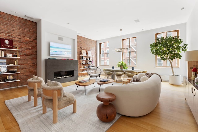 living room with light wood-style floors, a glass covered fireplace, and brick wall