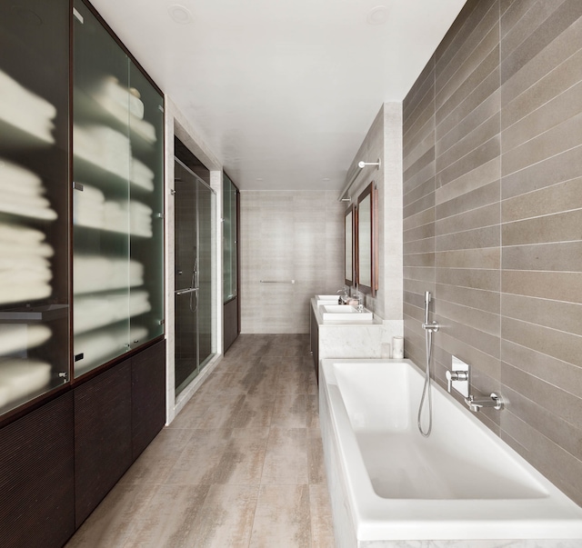 full bathroom featuring tiled bath, a shower with shower door, tile walls, and vanity