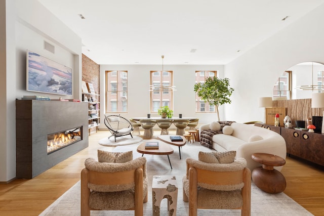 living area with a glass covered fireplace, light wood-style floors, and a chandelier