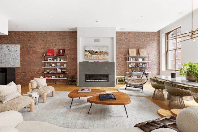 living room featuring a glass covered fireplace, brick wall, and wood finished floors