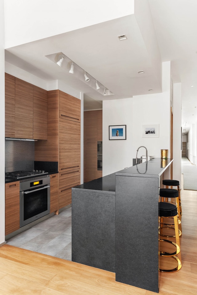 kitchen with dark countertops, visible vents, stovetop, stainless steel oven, and brown cabinets