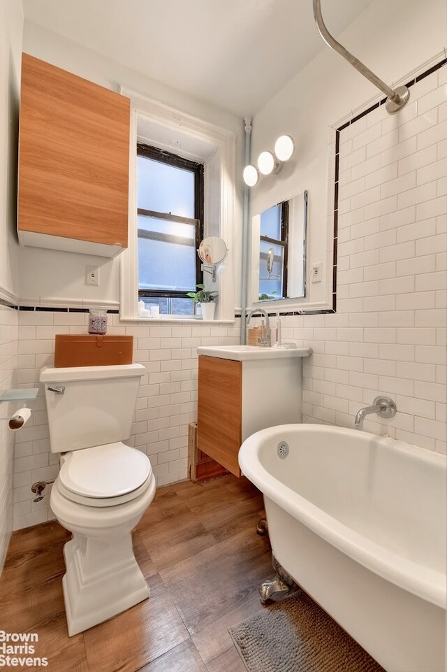 bathroom with toilet, tile walls, a tub to relax in, and hardwood / wood-style floors