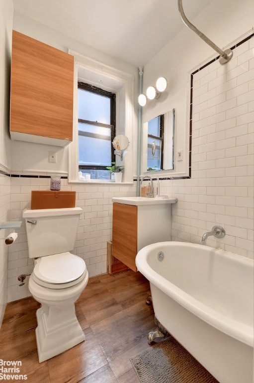 bathroom with tile walls, a tub to relax in, vanity, and toilet