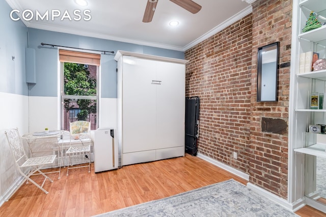 interior space with crown molding, ceiling fan, wood finished floors, and brick wall