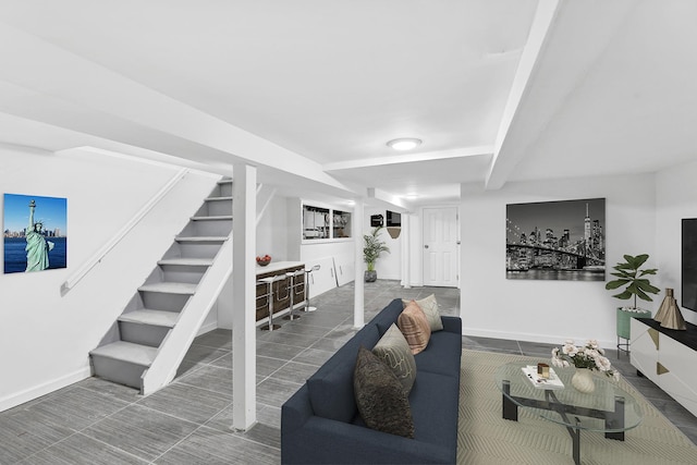 living room featuring baseboards, beam ceiling, and stairway
