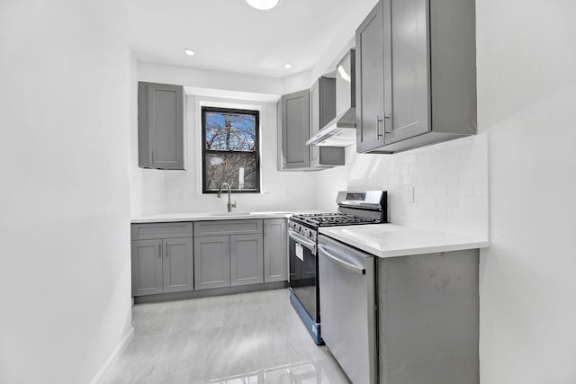 kitchen with wall chimney exhaust hood, stainless steel appliances, a sink, backsplash, and gray cabinets