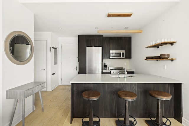 kitchen featuring sink, a breakfast bar area, kitchen peninsula, stainless steel appliances, and light hardwood / wood-style flooring