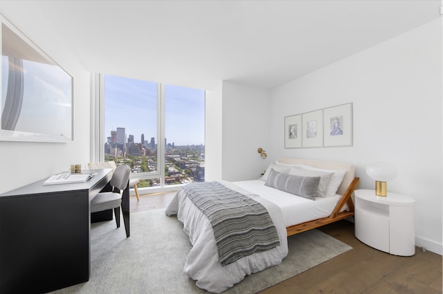 bedroom with a view of city, expansive windows, and wood finished floors