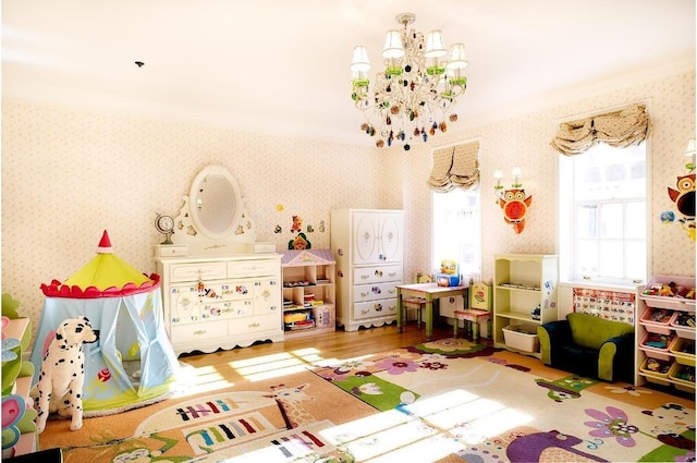 playroom featuring wood-type flooring, ornamental molding, and an inviting chandelier