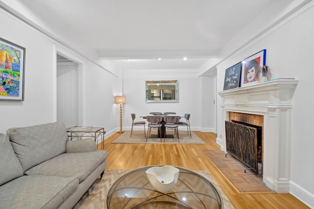 living room featuring a tiled fireplace, beam ceiling, and wood-type flooring