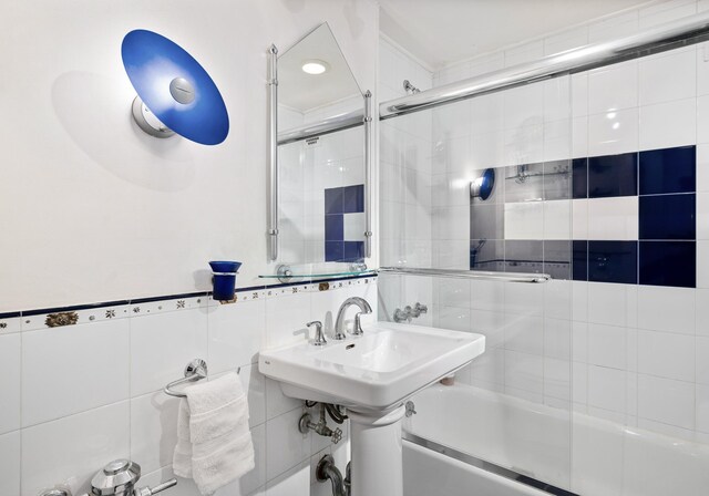 bathroom with tile walls and shower / bath combination with glass door