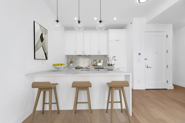 kitchen with a breakfast bar, kitchen peninsula, white cabinets, and decorative light fixtures