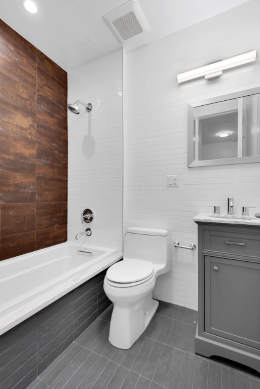 full bathroom with toilet, tiled shower / bath, tile walls, vanity, and tile patterned flooring