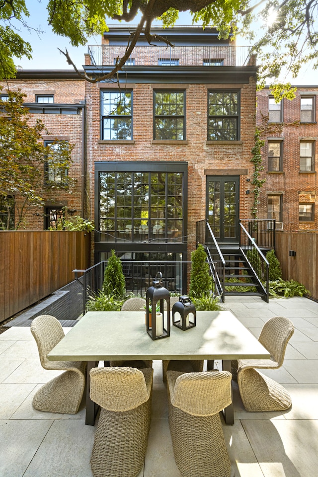 back of property with outdoor dining area, brick siding, french doors, and fence