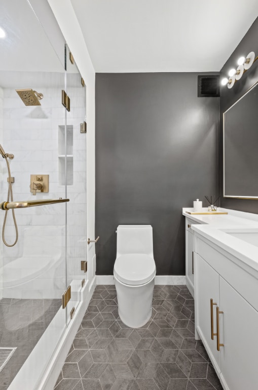 bathroom with a shower with door, vanity, tile patterned floors, and toilet