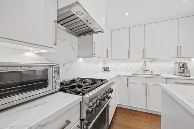 kitchen featuring a sink, white cabinets, range hood, light stone countertops, and stainless steel range