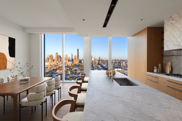 kitchen featuring light brown cabinetry, sink, stainless steel gas cooktop, hardwood / wood-style flooring, and a wall of windows