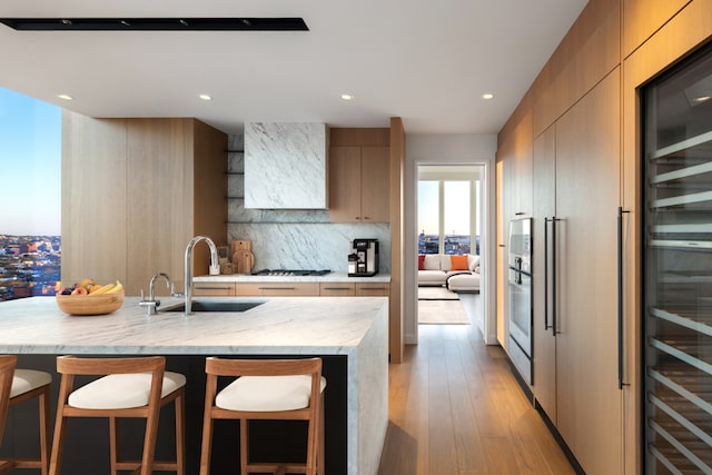 kitchen featuring wine cooler, light brown cabinetry, sink, light stone counters, and decorative backsplash