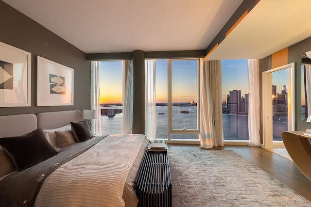 bedroom featuring access to exterior, wood finished floors, and a water view