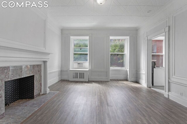 unfurnished living room featuring hardwood / wood-style floors, radiator, ornamental molding, and a fireplace