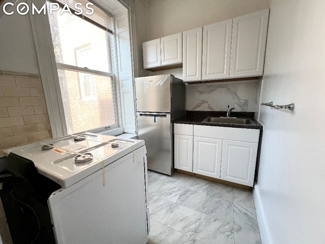 kitchen featuring white cabinets, sink, backsplash, stainless steel refrigerator, and white range