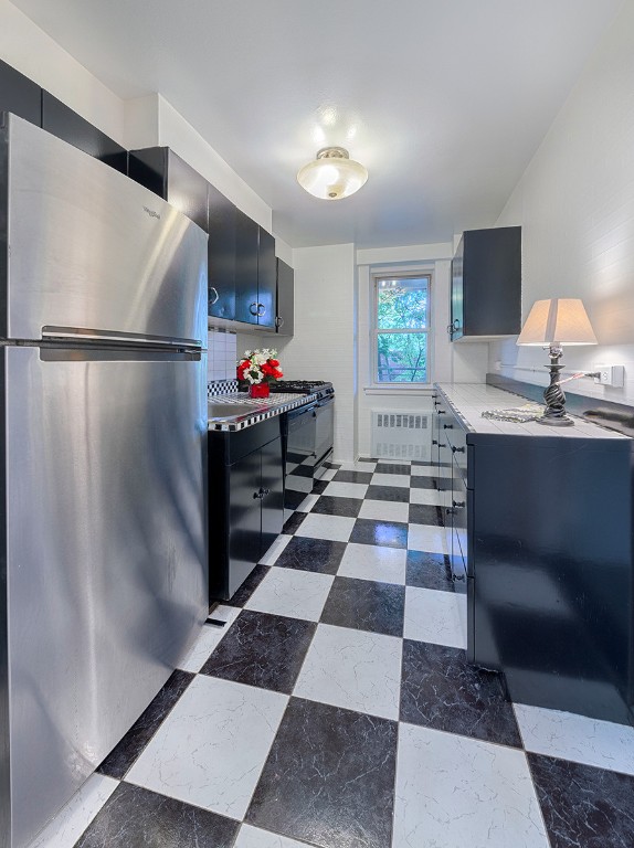 kitchen with black gas range oven, radiator, and stainless steel refrigerator