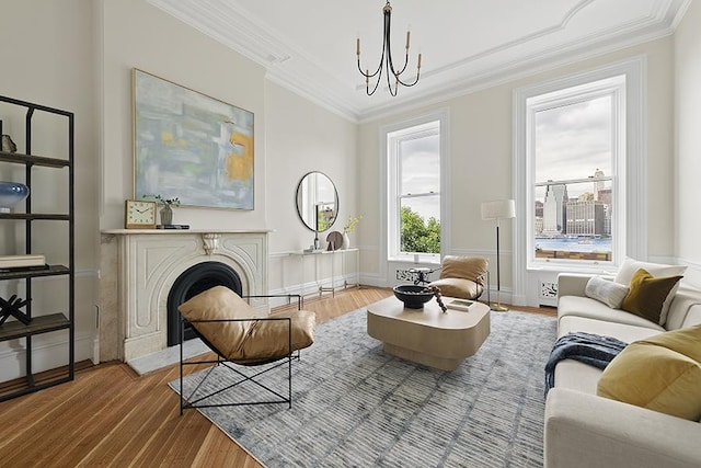 sitting room featuring wood finished floors, an inviting chandelier, a fireplace, crown molding, and baseboards