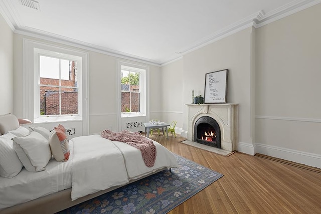 bedroom with visible vents, ornamental molding, wood finished floors, a lit fireplace, and baseboards