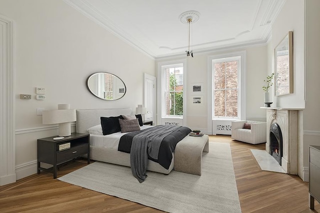 bedroom with a fireplace with flush hearth, crown molding, light wood-type flooring, and baseboards