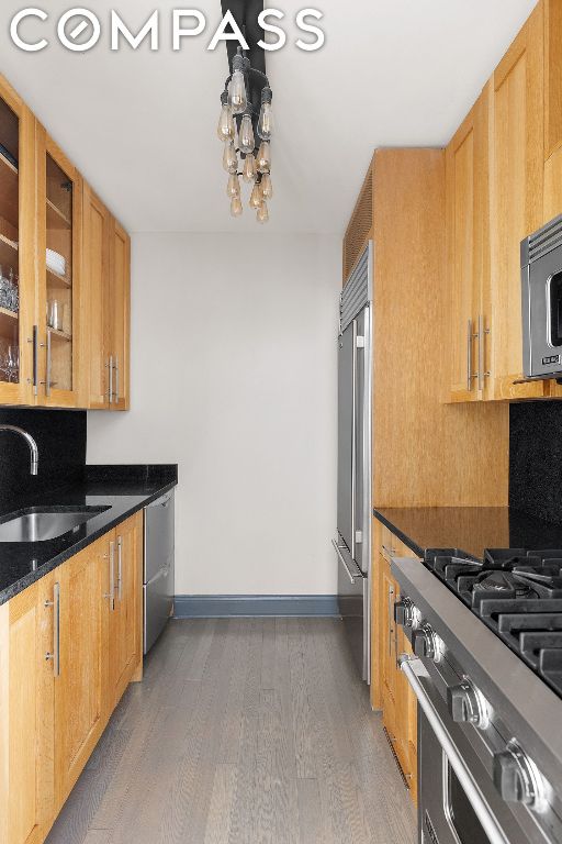 kitchen featuring dark wood-type flooring, stainless steel appliances, dark stone counters, and sink