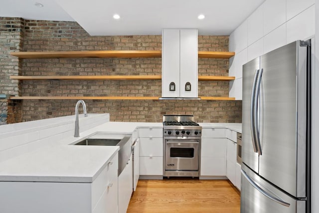 kitchen with brick wall, appliances with stainless steel finishes, white cabinetry, sink, and light hardwood / wood-style flooring