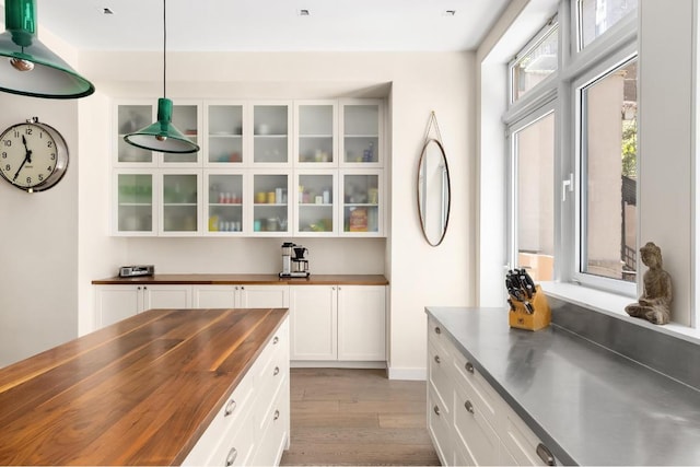 bar with hanging light fixtures, hardwood / wood-style flooring, wooden counters, and white cabinets