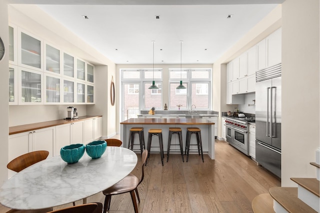 308 E 30th St Unit 1, New York City, NY 10016 - kitchen featuring high end appliances, light wood-style flooring, a kitchen breakfast bar, white cabinetry, and glass insert cabinets