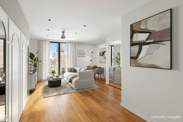 living room with a wall mounted air conditioner, ceiling fan, and light hardwood / wood-style floors