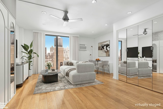 living room featuring a ceiling fan, a wall unit AC, a city view, light wood-style floors, and recessed lighting