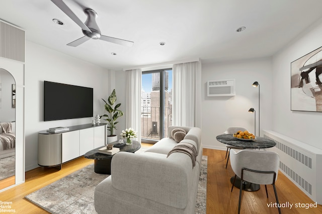 living room with arched walkways, a ceiling fan, a wall unit AC, radiator heating unit, and light wood-style flooring